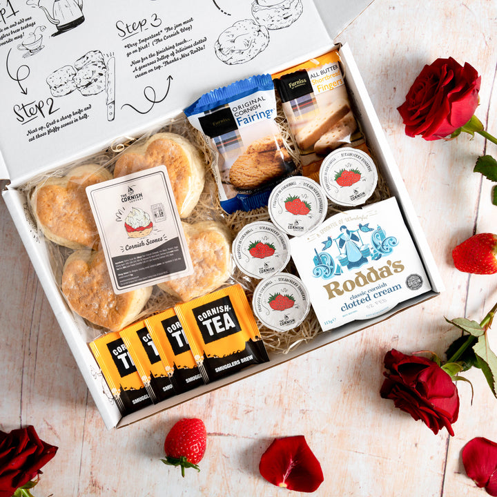 A cream tea hamper with love heart scones, placed on a wooden floor with roses laid out.